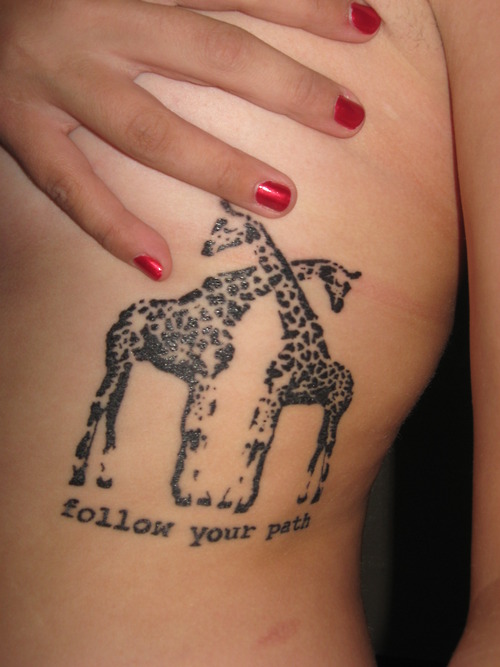 Giraffes standing in cross position with wording follow your path tattoo on rib cage
