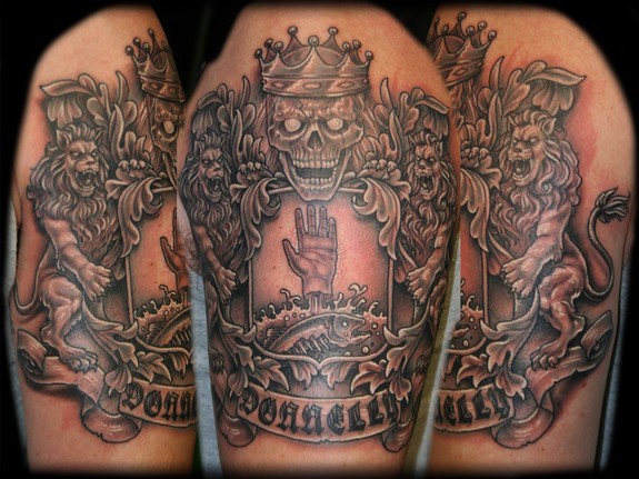 Black And Grey Hand In Skull Family Crest Tattoo On Man Shoulder