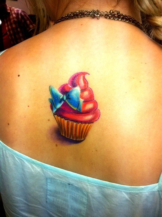 Red Cupcake With Blue Bow Tattoo On Girl Upper Back