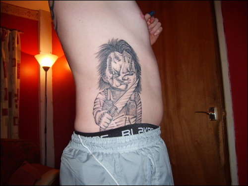 Black And Grey Knife On Chucky Hand Tattoo On Side Rib