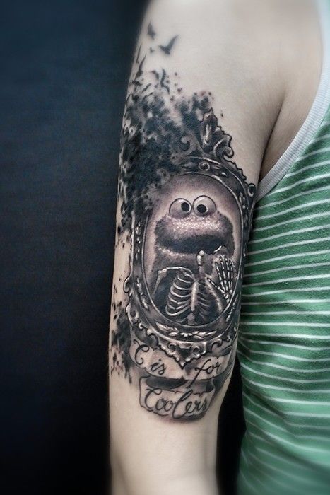 Black And Grey Monster In Frame With Banner Tattoo On Bicep