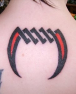 Black And Red Tribal Vampire Fangs Tattoo On Girl Upper Back