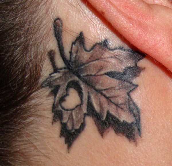 Black And Grey Heart In Maple Leave Tattoo On Behind The Ear