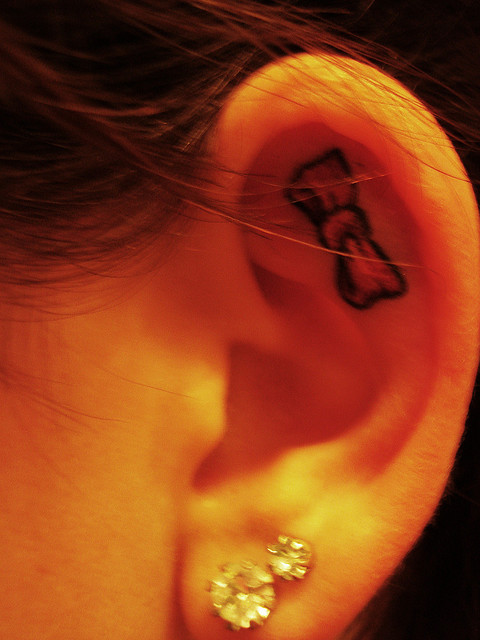 Black Bow Tattoo On Girl Inside The Ear