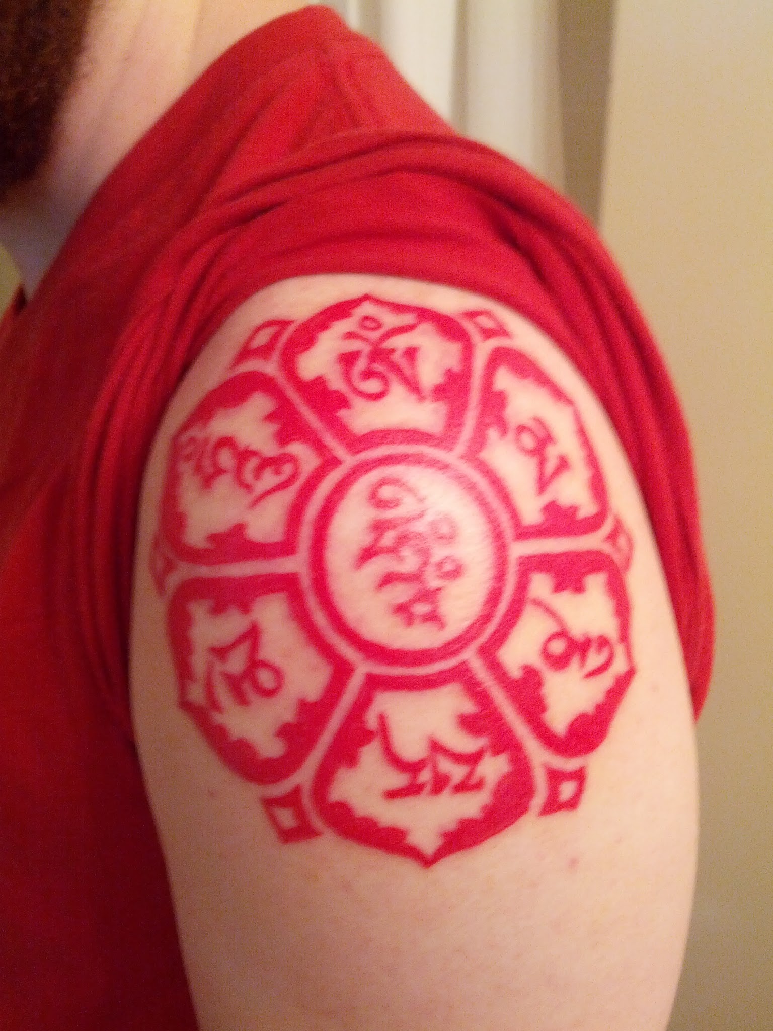 Red Buddhist Symbol Tattoo On Left Shoulder
