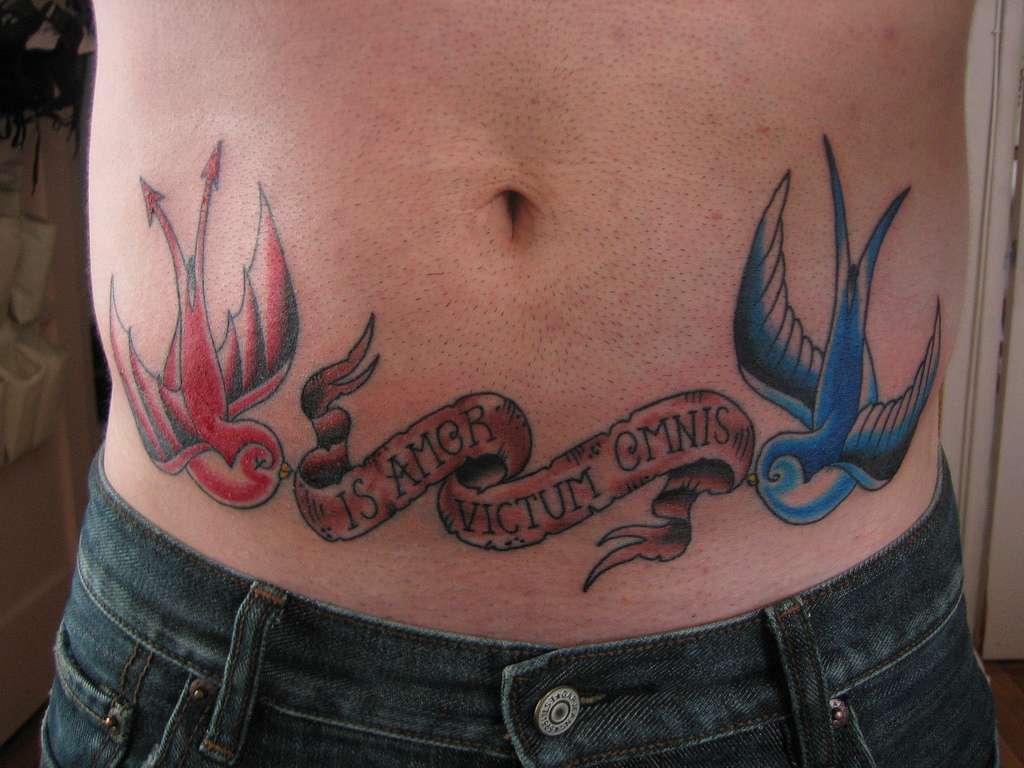 Blue And Red Two Flying Birds With Banner Tattoo On Lower Stomach