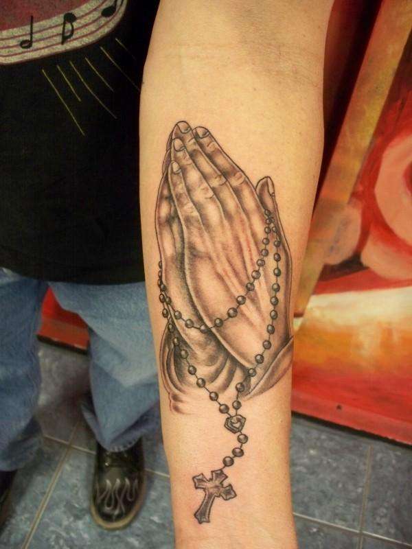 Grey Ink Rosary Cross In Praying Hand Tattoo On Forearm