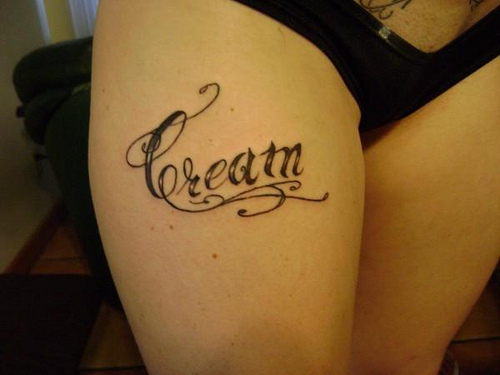Black Cream Lettering Tattoo On Right Thigh