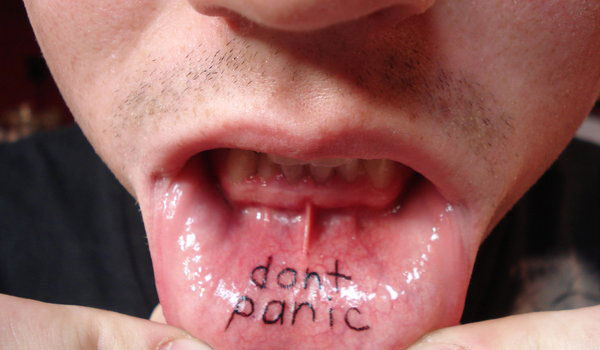 Black Don't Panic Lettering Tattoo On Man Inner Lip