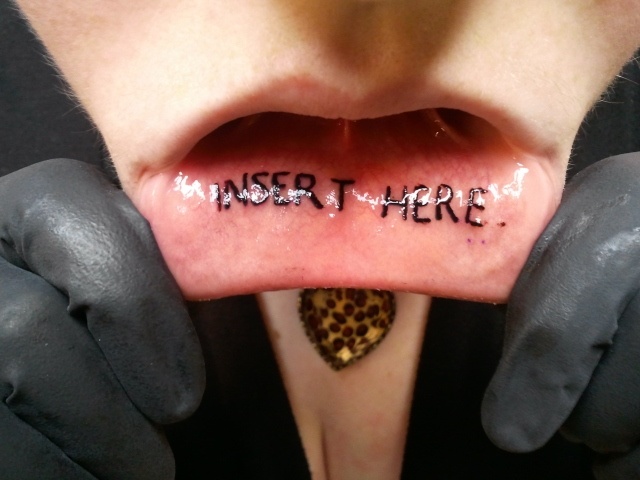 Black Insert Here Lettering Tattoo On Girl Inner Lip