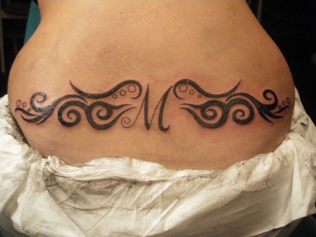 Black M With Swirl Tattoo On Lower Back