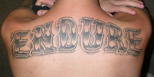 Grey Ink Endure Lettering Tattoo On Upper Back