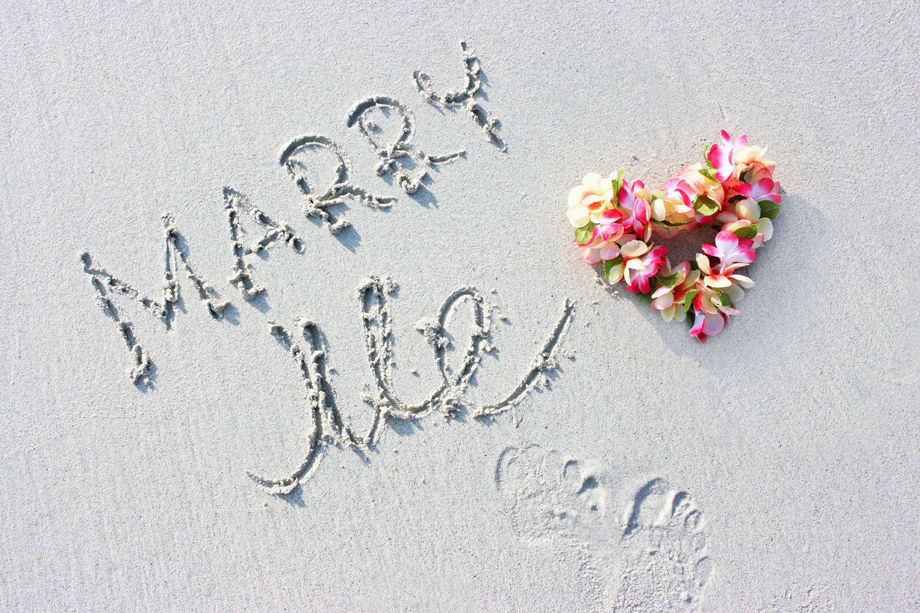 Marry Me Written On Sand With Flowers Heart
