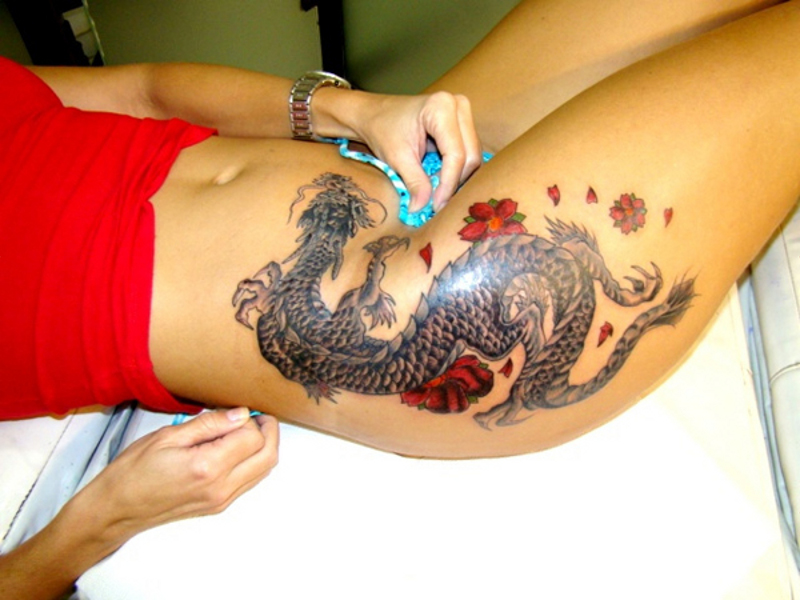 Black Ink Dragon With Red Flowers Tattoo On Girl Side Hip