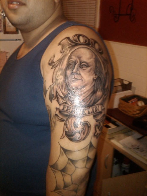 Black And Grey Greek Face With Banner And Web Tattoo On Left Half Sleeve