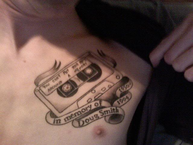 Black Ink Cassette With Banner Tattoo On Chest