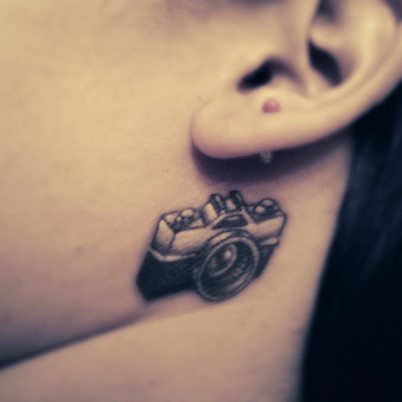Amazing Black Ink Camera Tattoo On Behind The Ear