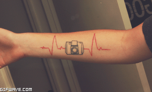 Camera With Red Heartbeat Tattoo On Forearm