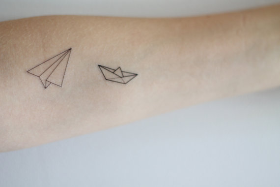 Black Outline Paper Boat And Plane Tattoo On Forearm