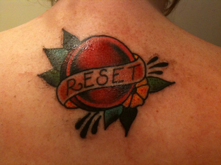 Reset Button With Banner Tattoo On Upper Back