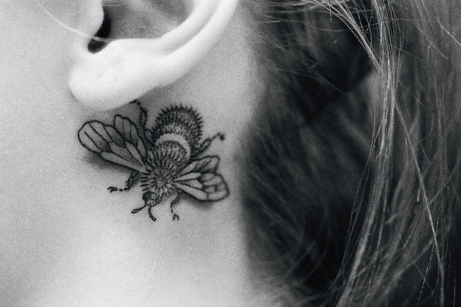 Black And Grey Bumblebee Tattoo On Girl Behind The Ear