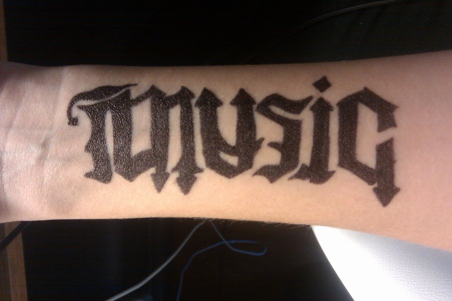Black Ambigram Music Lettering Tattoo On Forearm By Liz