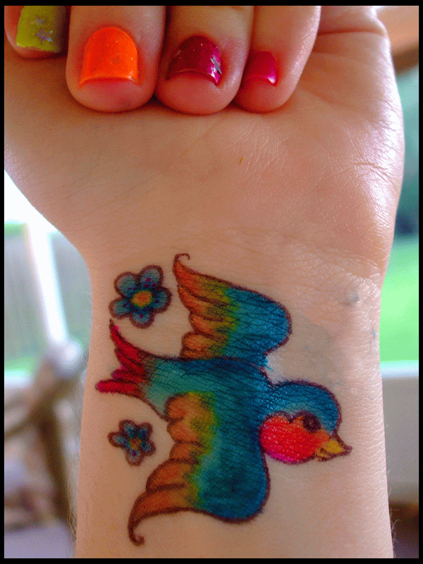 Colorful Bird With Flowers Tattoo On Girl Wrist By Hadley Dablur Hansen