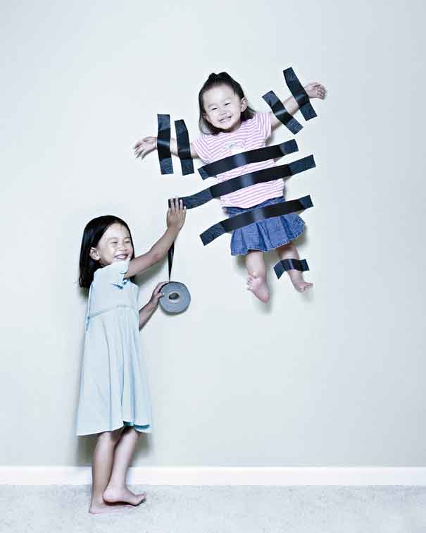Funny Girl Fixing Her Little Sister On Wall With Duct Tape