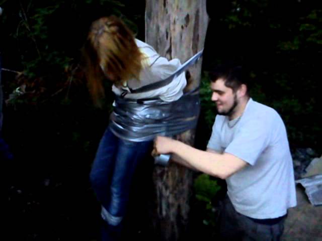 Funny Man Wrapping Girl With Tree Using Duct Tape