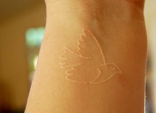 Outline Flying Bird White Ink Tattoo On Wrist