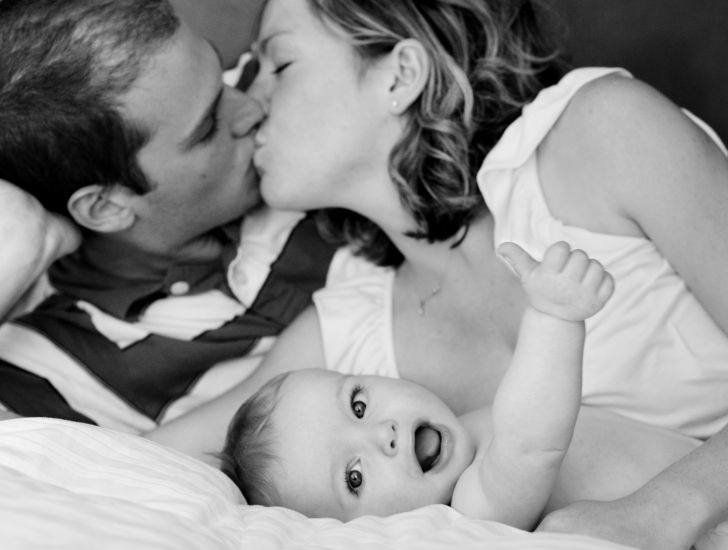 Parents Kissing Funny Baby Showing Thumbs