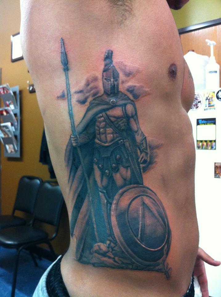 Black And Grey Ink Spartan Tattoo On Man Rib Side