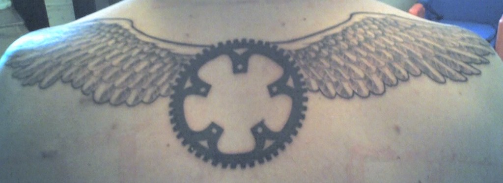 Black Mountain Bike Sprocket With Wings Tattoo On Upper Back