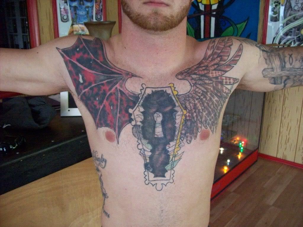 Man Showing His Angel And Devil Winged Coffin Tattoo On Chest
