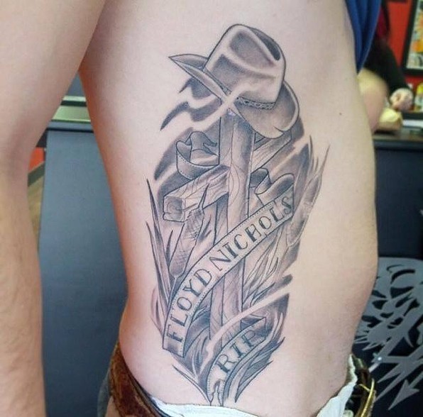 Grey Ink Cross With Cowboy Hat And Banner Tattoo Design For Side Rib
