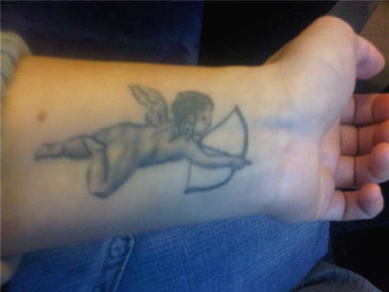 Black And Grey Bow And Arrow In Cupid Cherub Hand Tattoo On Forearm