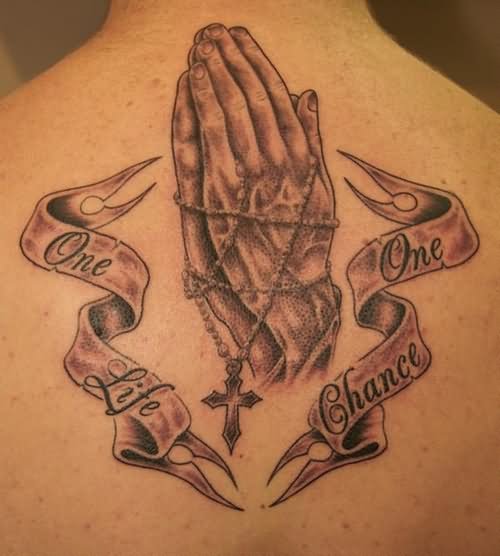 Black Ink Praying Hands With Words Ribbon Tattoo On Upper Back