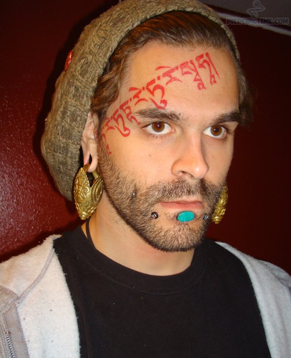 Red Ink Sanskrit Tattoo On Guy Forehead