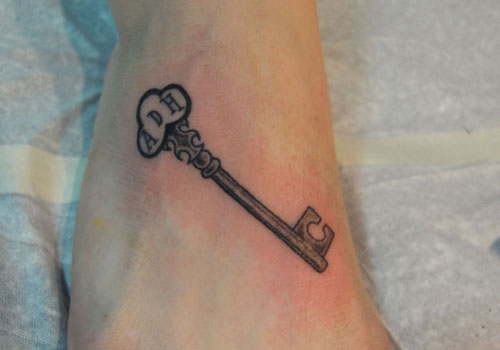 Simple Black Ink Key Tattoo Design For Foot