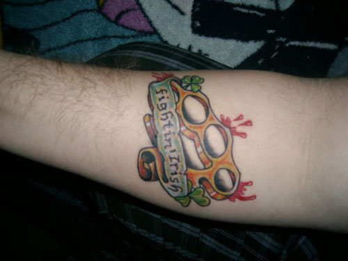 Brass Knuckle And Fighting Irish Banner Tattoo On Forearm