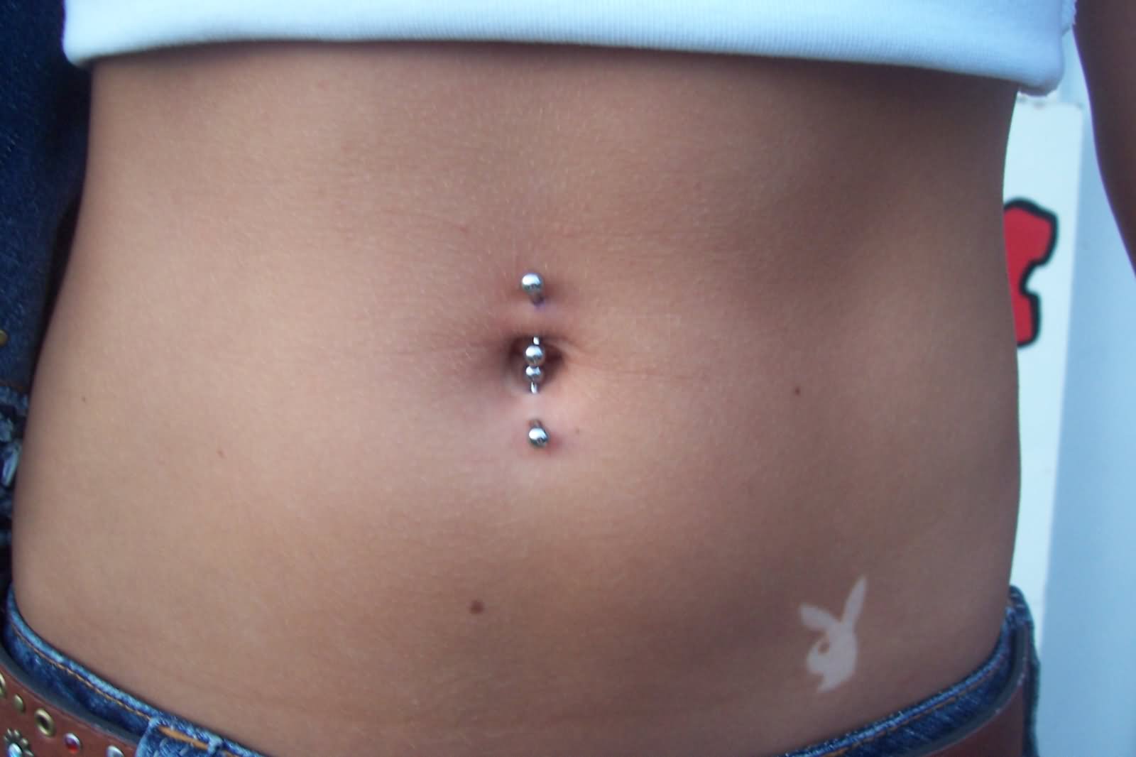 Silver Barbells Belly Piercing And Playboy Bunny Hip Tattoo