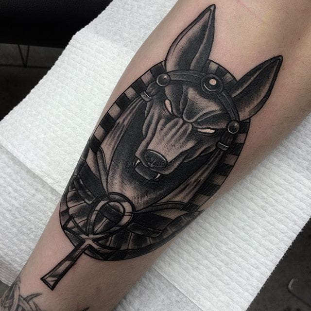 Black And Grey Anubis Head With Ankh Tattoo On Leg