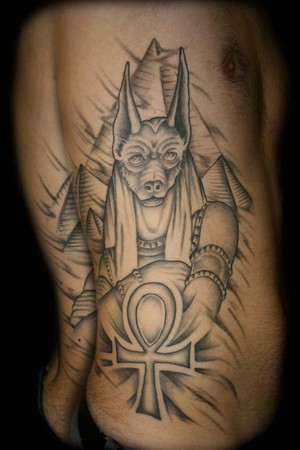 Grey Ink Ankh And Anubis Tattoo On Man Side Rib