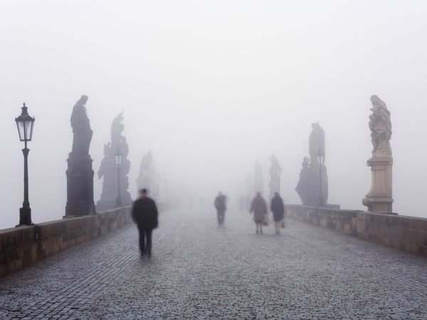 Pedestrians Walking On Charles Bridge During A Foggy Morning
