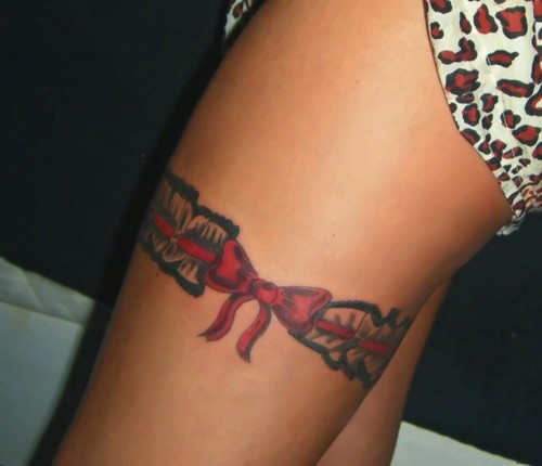 Red Bow And Black Ink Garter Tattoo On Thigh