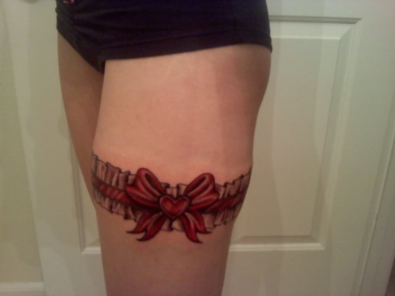 Red Ink Bow Garter Tattoo On Thigh