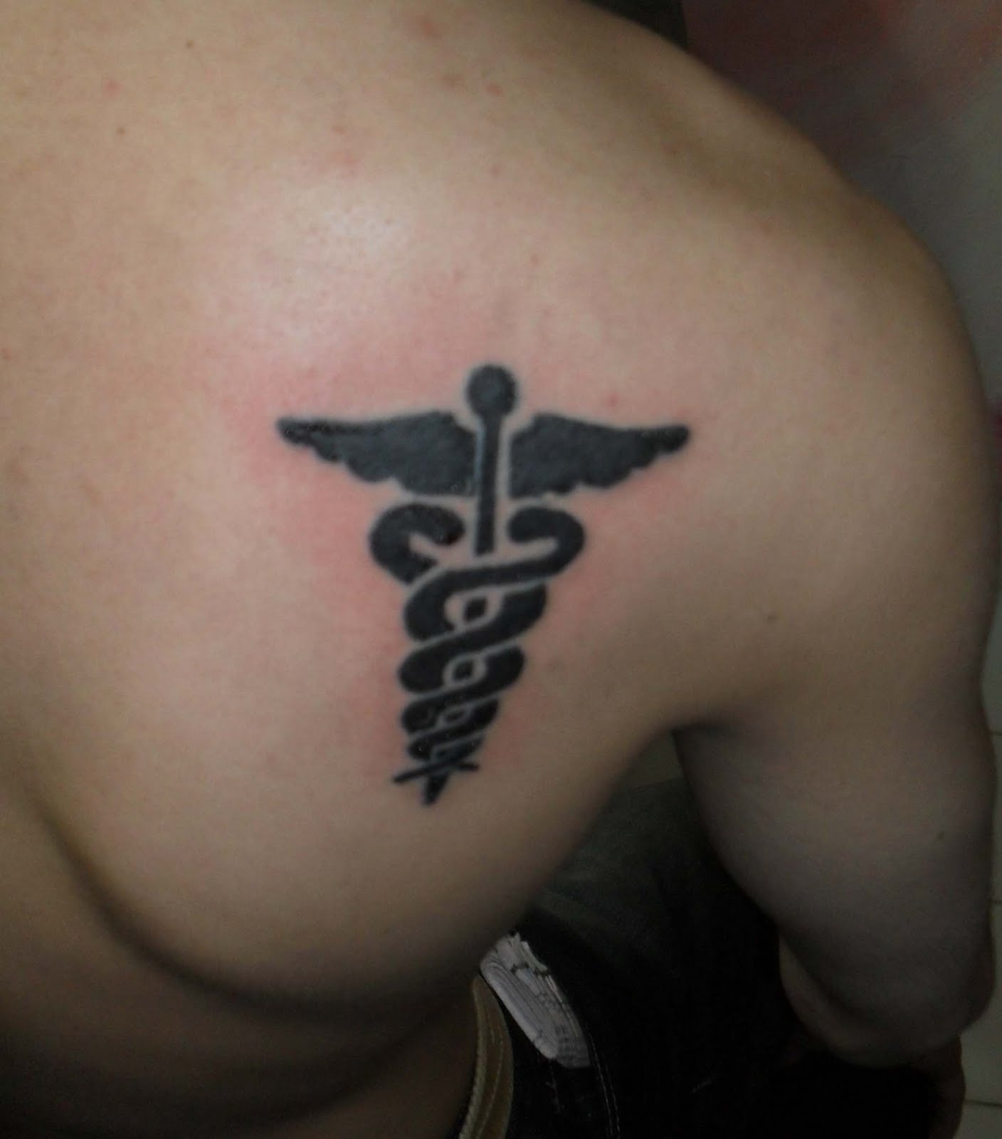 Black Medical Symbol Tattoo On Upper Right Back
