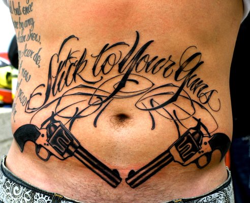 Stick To Your Guns Lettering With Two Guns Tattoo On Stomach