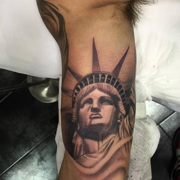 Black Ink Statue Of Liberty Face Tattoo On Bicep
