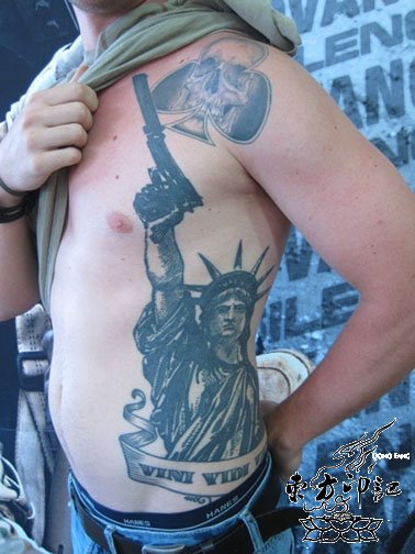 Black Ink Statue Of Liberty With Gun And Banner Tattoo On Man Left Side Rib